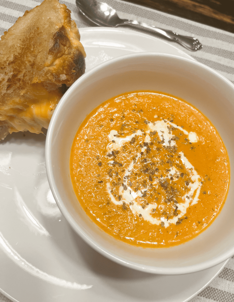 Creamy Roasted Tomato Soup in a bowl with a sourdough grilled cheese sandwich