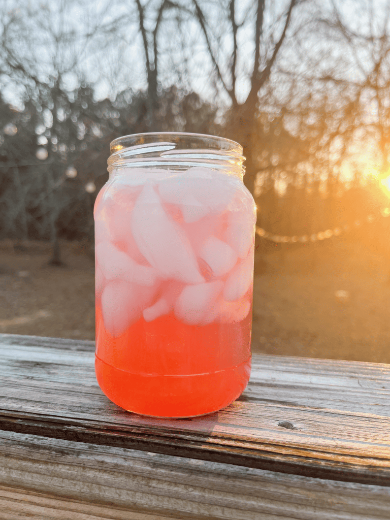 Cranberry Ginger Ale on wood plank with sunset in the background