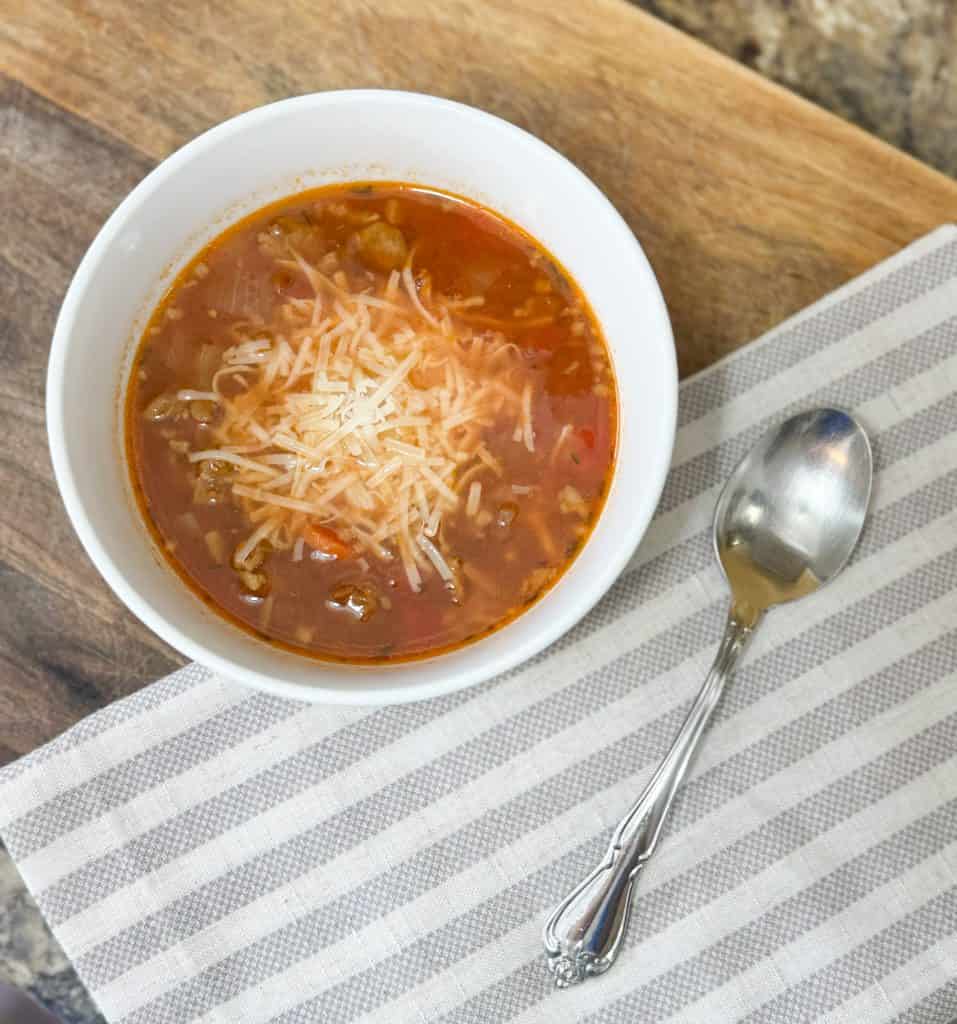 lentil soup in a white bowl on a wooden cutting board with a spoon lying next to the bowl