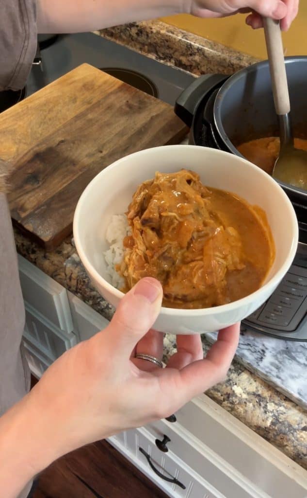 ladling butter chicken out of an instant pot over a bowl of rice