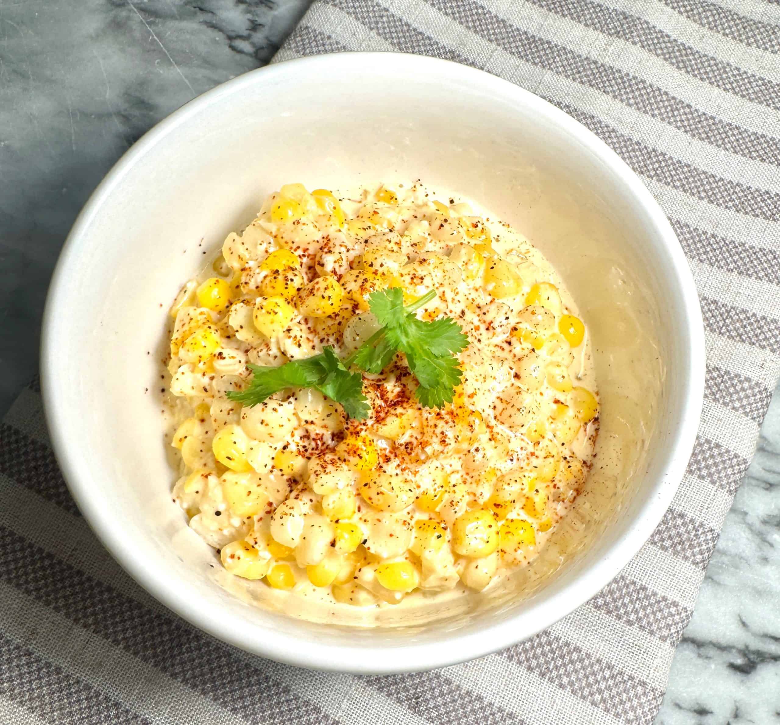 mexican street corn in a white bowl garnished with cilantro and chili powder