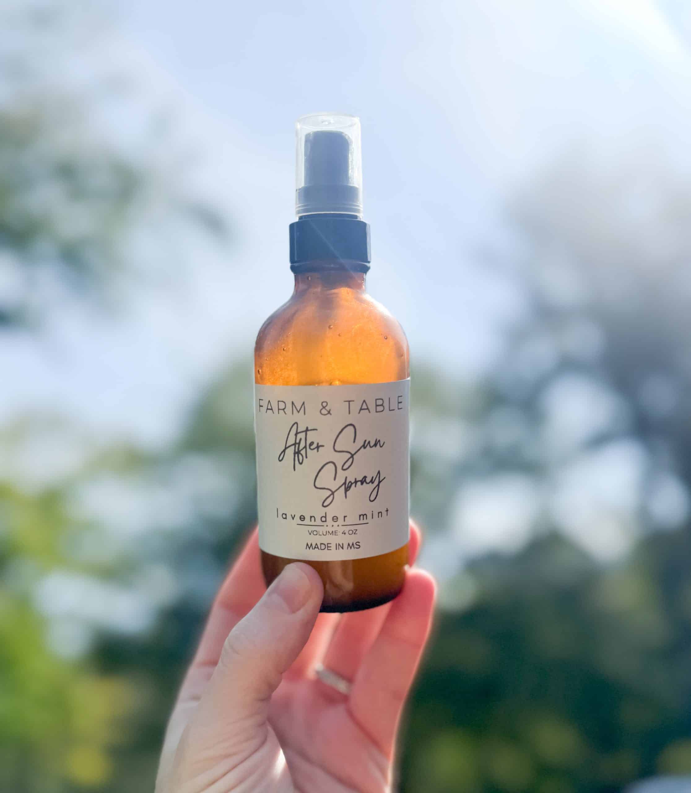 after sun spray in a 4 ounce amber bottle being held up outside with trees and the sun in the background