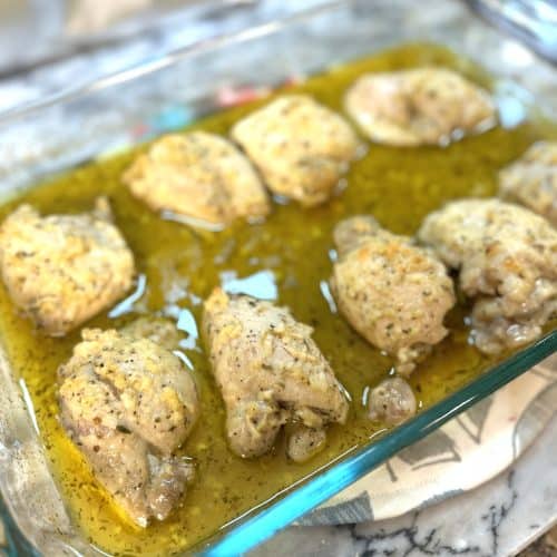 baked greek lemon chicken in a glass casserole dish sitting on a marble board