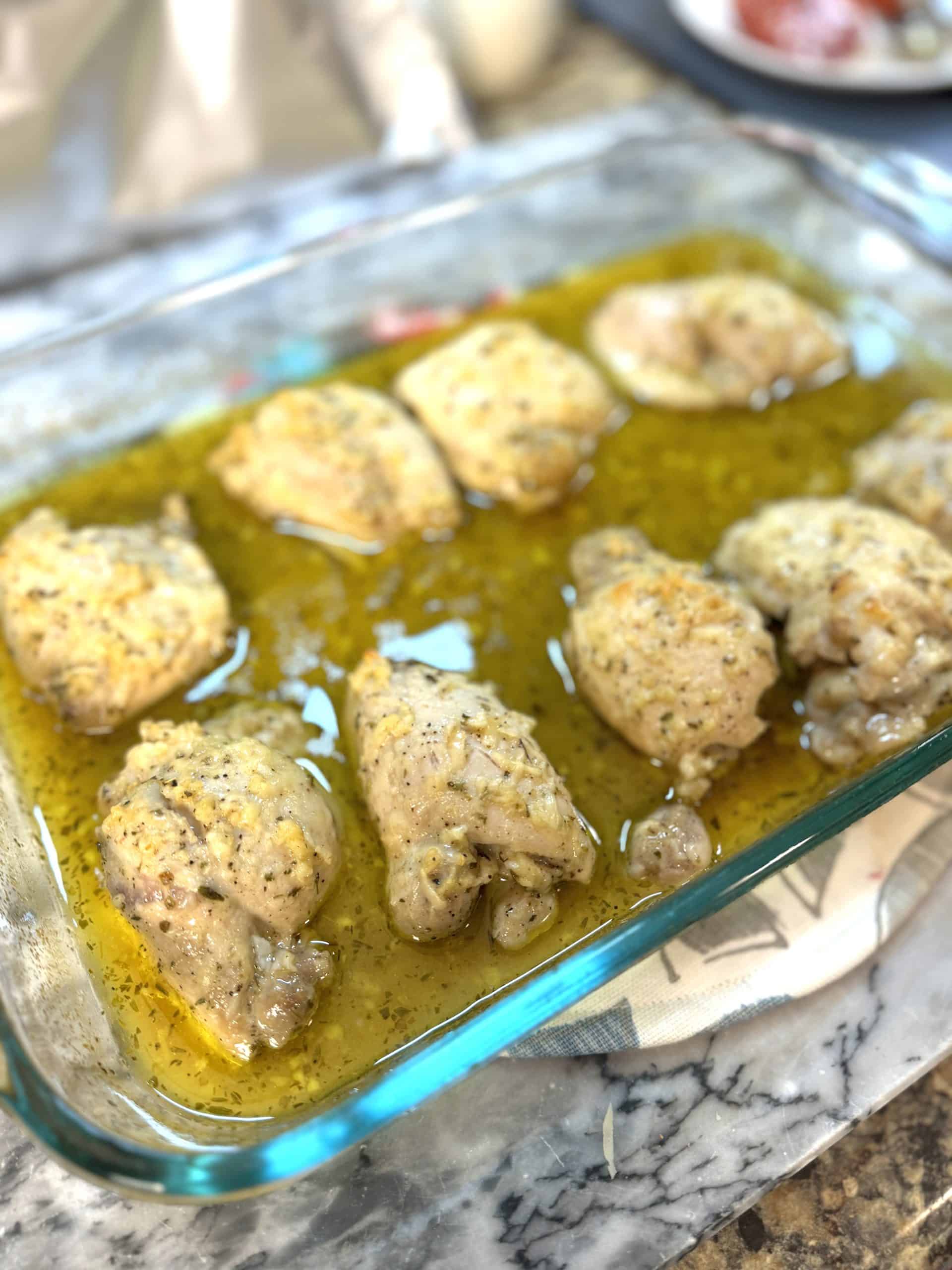 baked greek lemon chicken in a glass casserole dish sitting on a marble board
