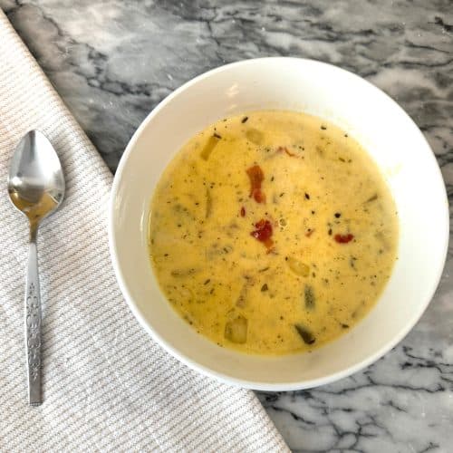 beer and cheddar soup in a white bowl on a marble counter next to a cloth napkin and a spoon