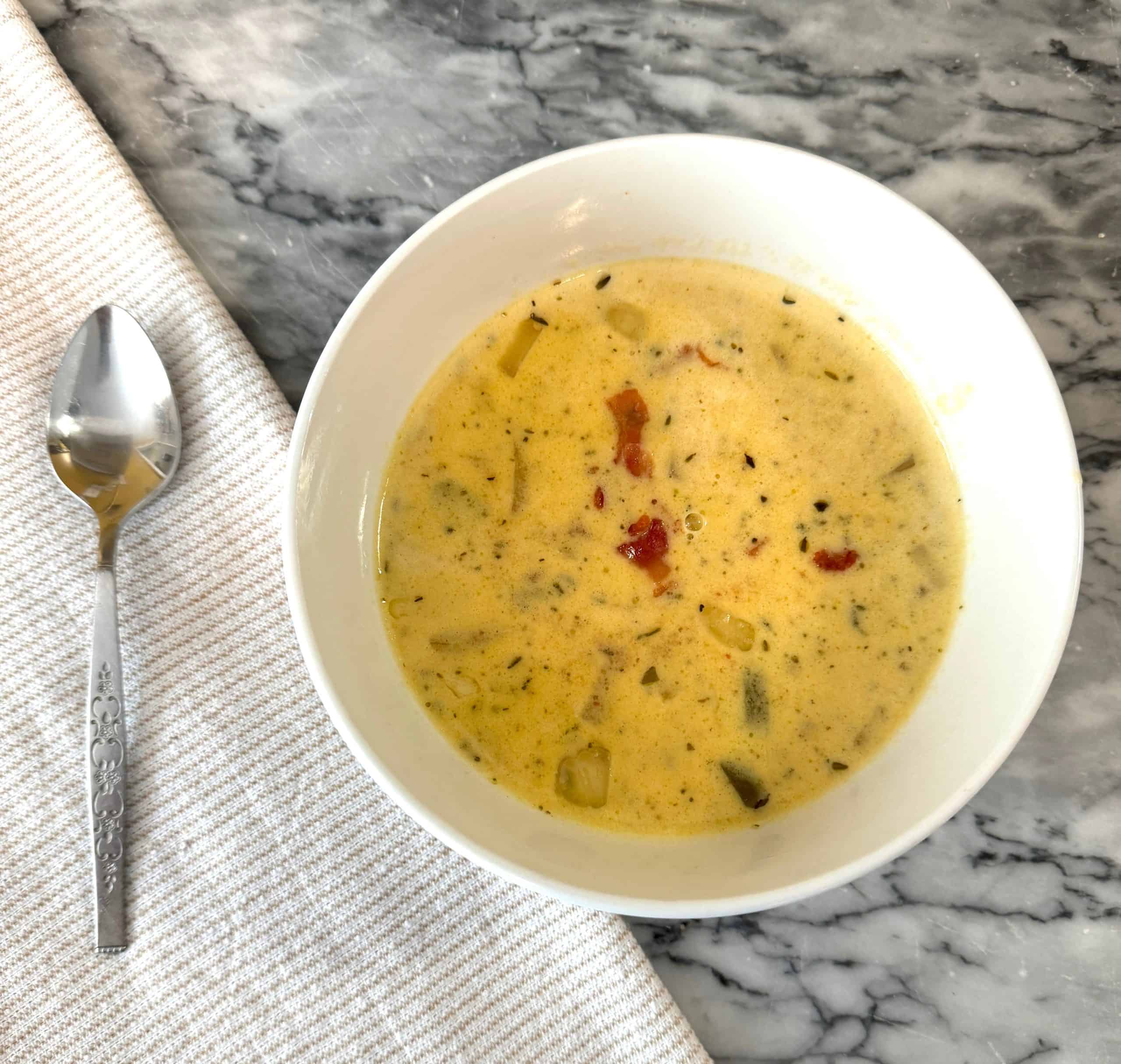beer and cheddar soup in a white bowl on a marble counter next to a cloth napkin and a spoon