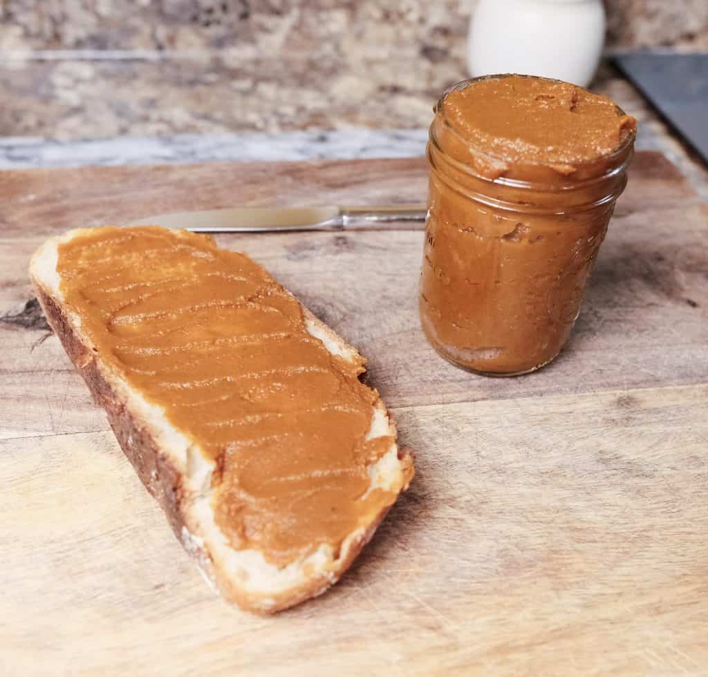 Homemade pumpkin butter spread on a slice of toast next to a mason jar filled with pumpkin butter on a wooden surface