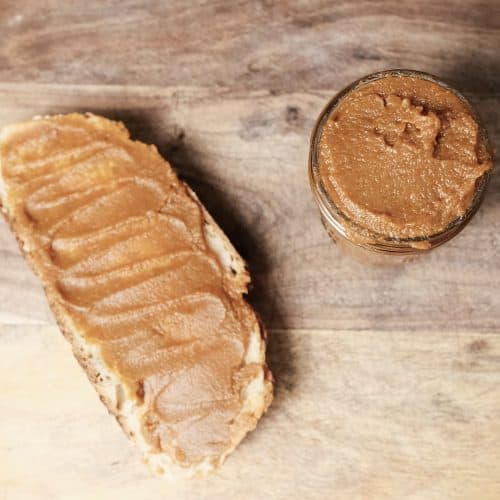 Homemade pumpkin butter spread on a slice of toast next to a mason jar filled with pumpkin butter on a wooden surface