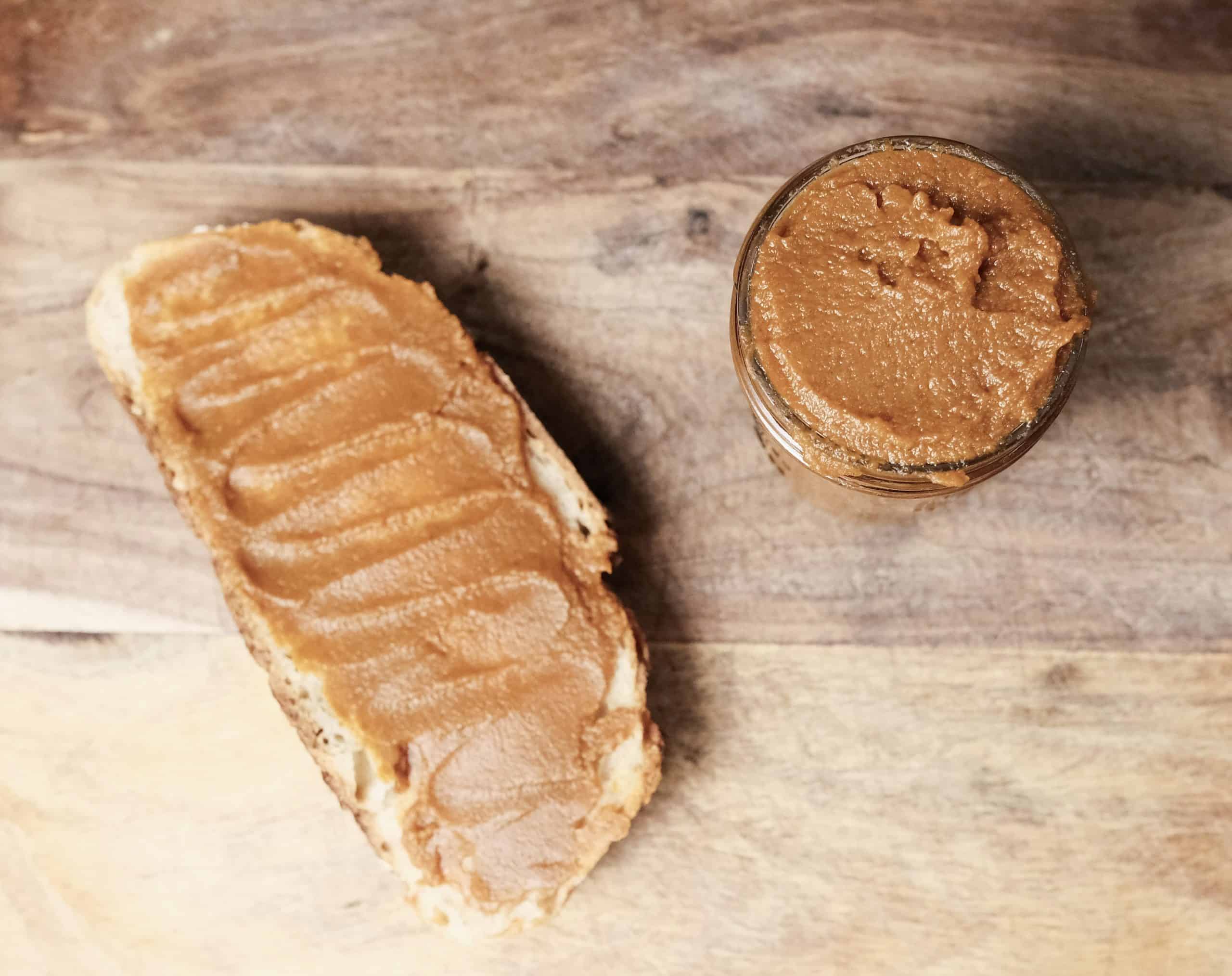 Homemade pumpkin butter spread on a slice of toast next to a mason jar filled with pumpkin butter on a wooden surface