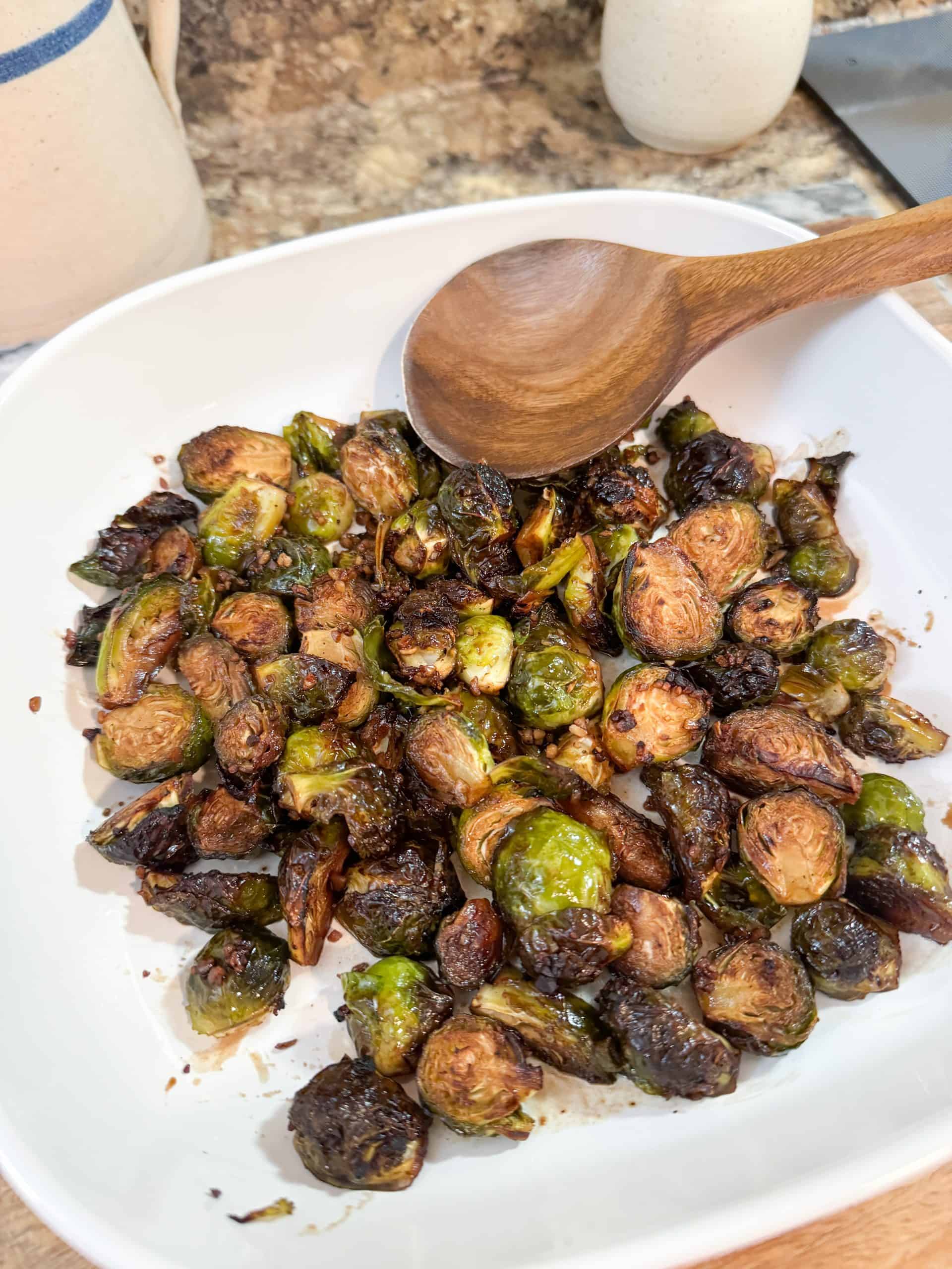 Balsamic Honey Glazed Brussels Sprouts in a white casserole dish with a wooden spoon