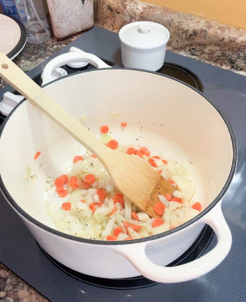 carrots and onions being cooked in a large dutch oven