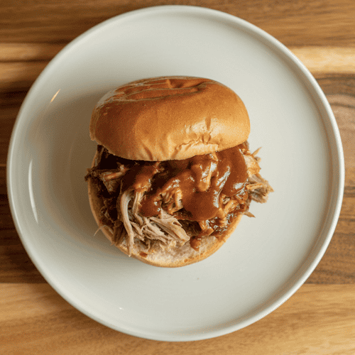 Instant Pot Barbecue Pulled Pork Sandwich on a white plate sitting on a wooden cutting board