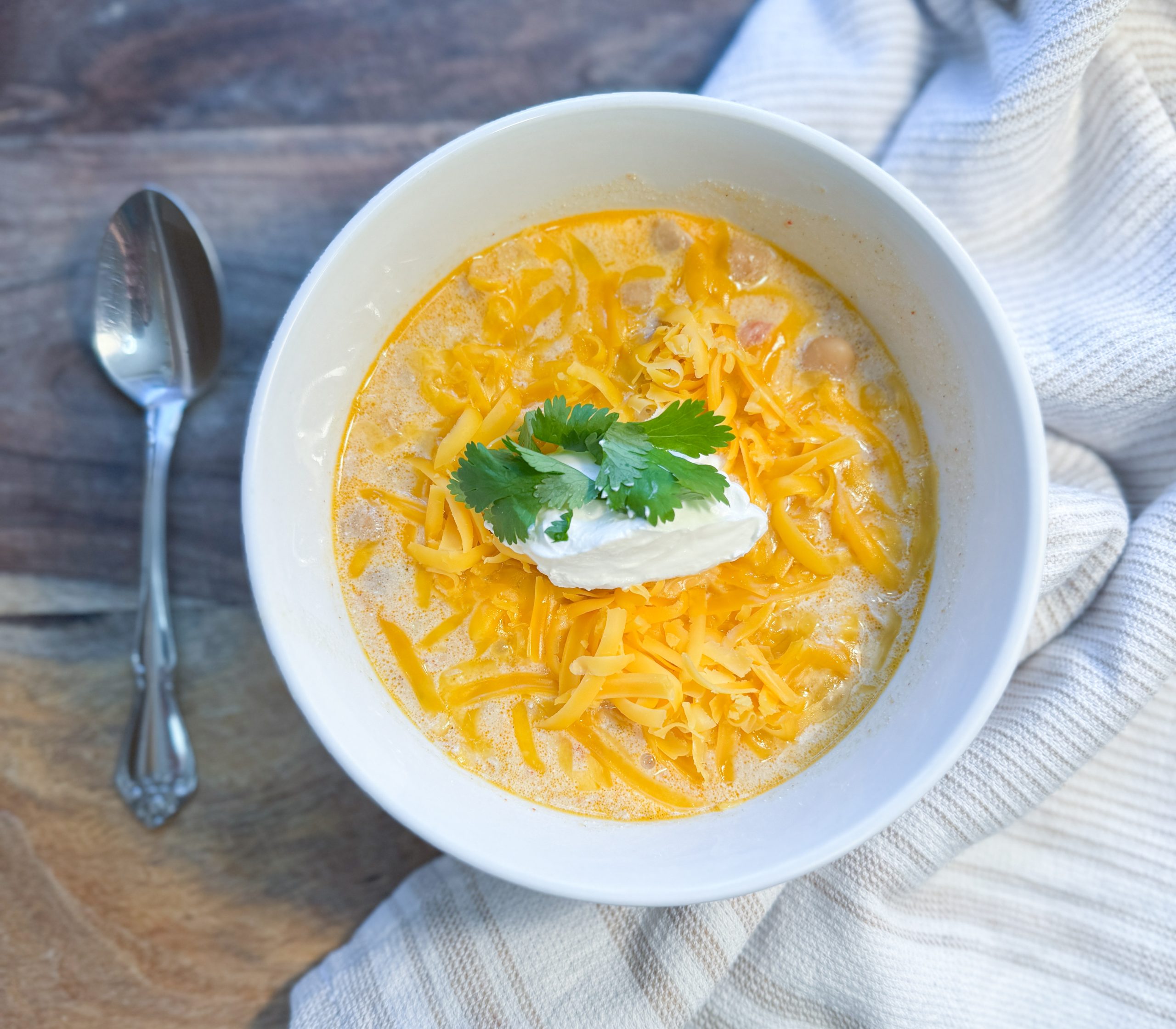white chicken chili in a bowl sitting on a wooden cutting board next to a spoon