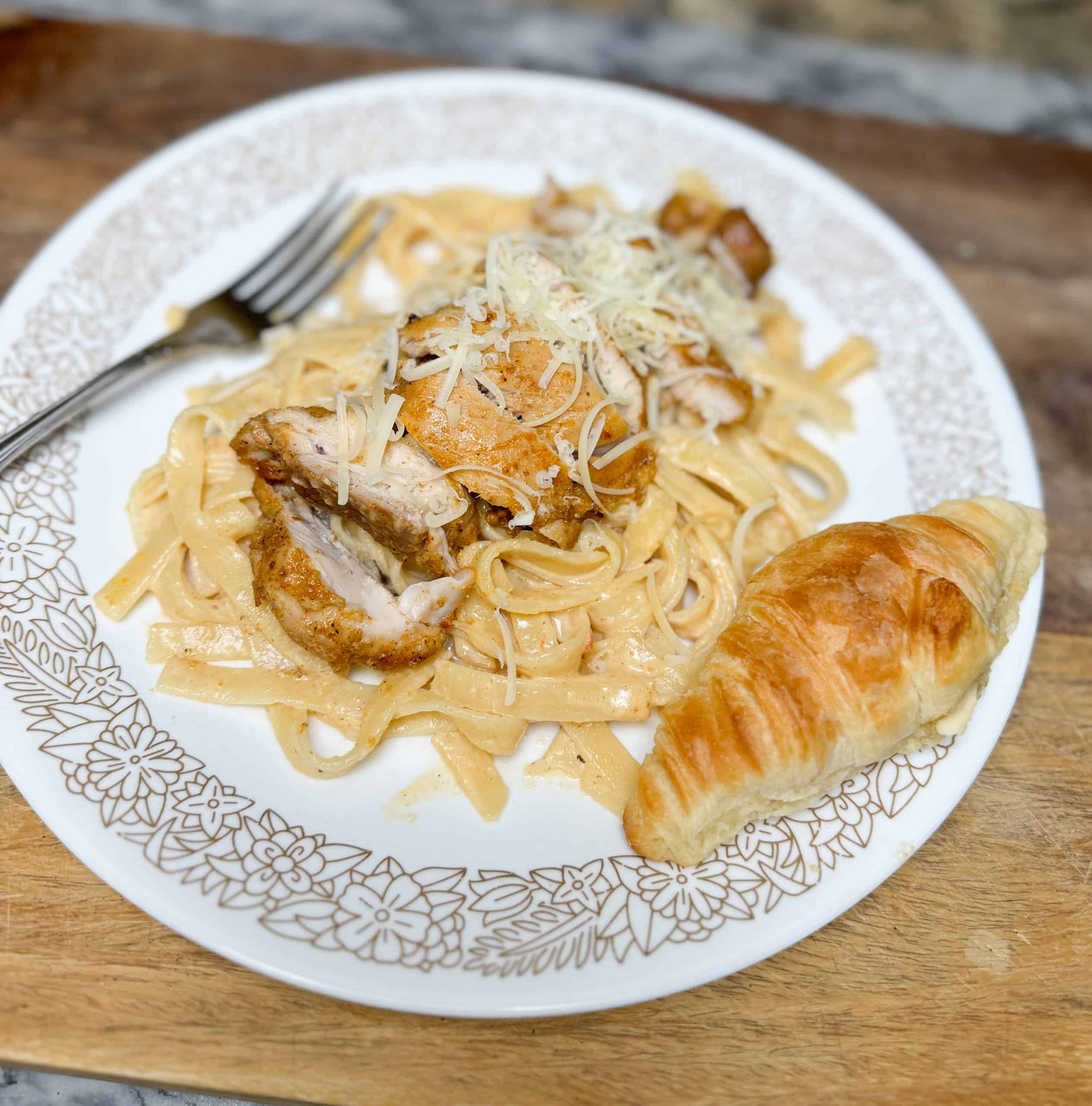 Creamy Chicken Fettuccine with Tomatoes and Parmesan on a plate sitting on a wooden cutting board