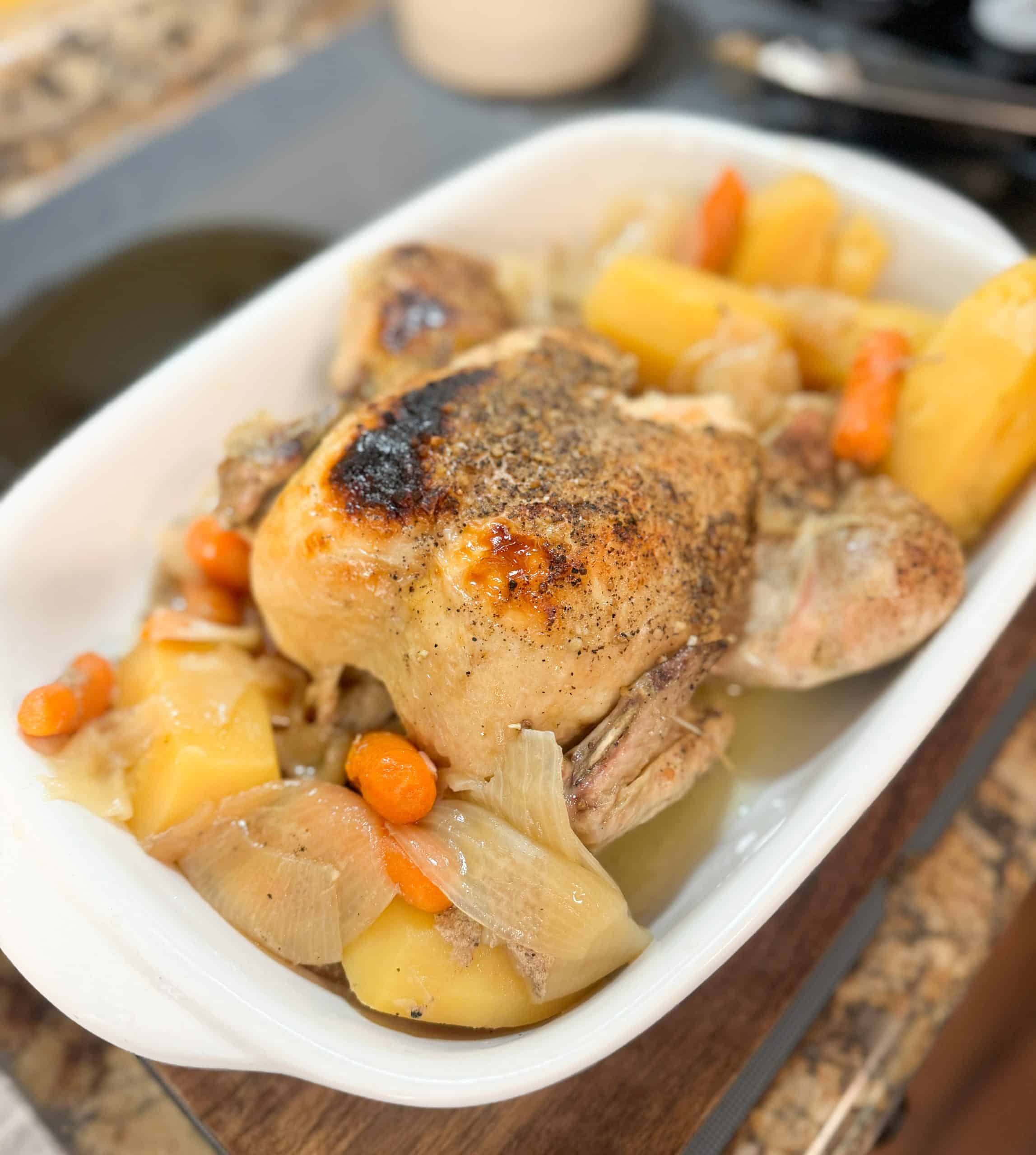 a whole chicken in a casserole dish surrounded by potatoes, carrots and onions