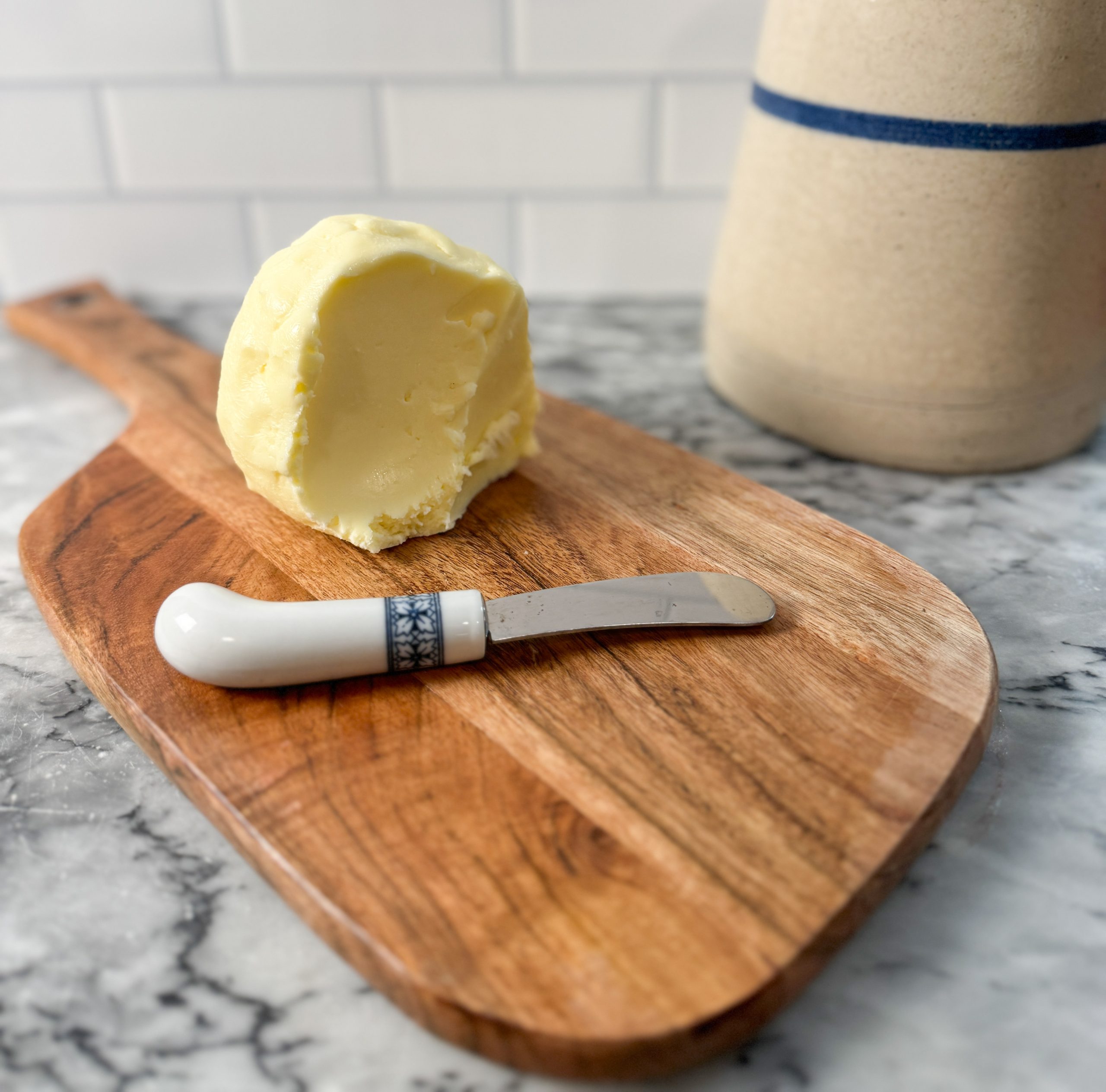 homemade butter in a ball on a wood cutting board next to a butter knife