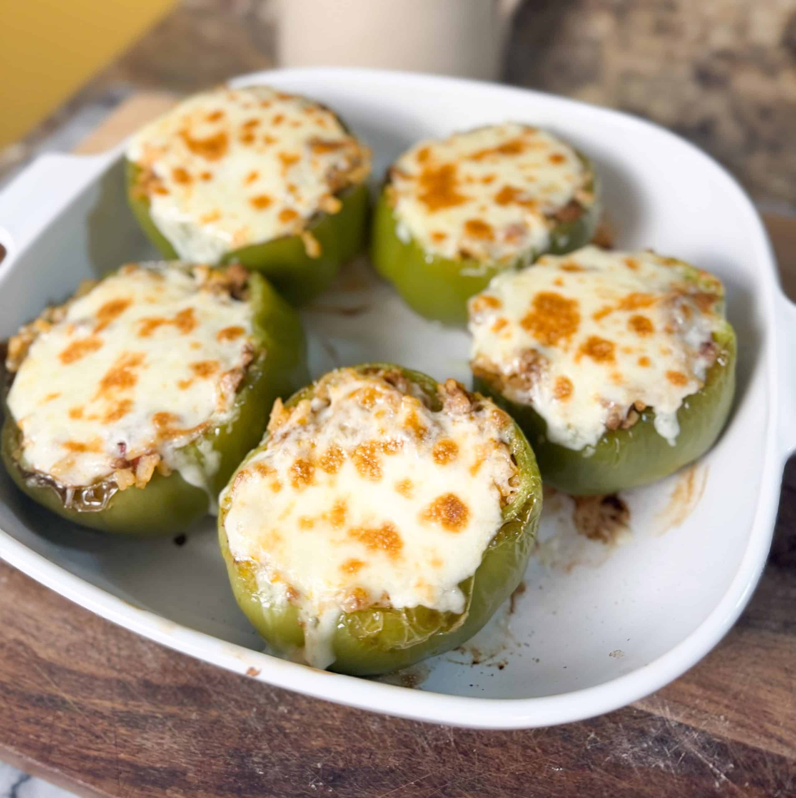 stuffed bell peppers in a casserole dish sitting on a wooden cutting board