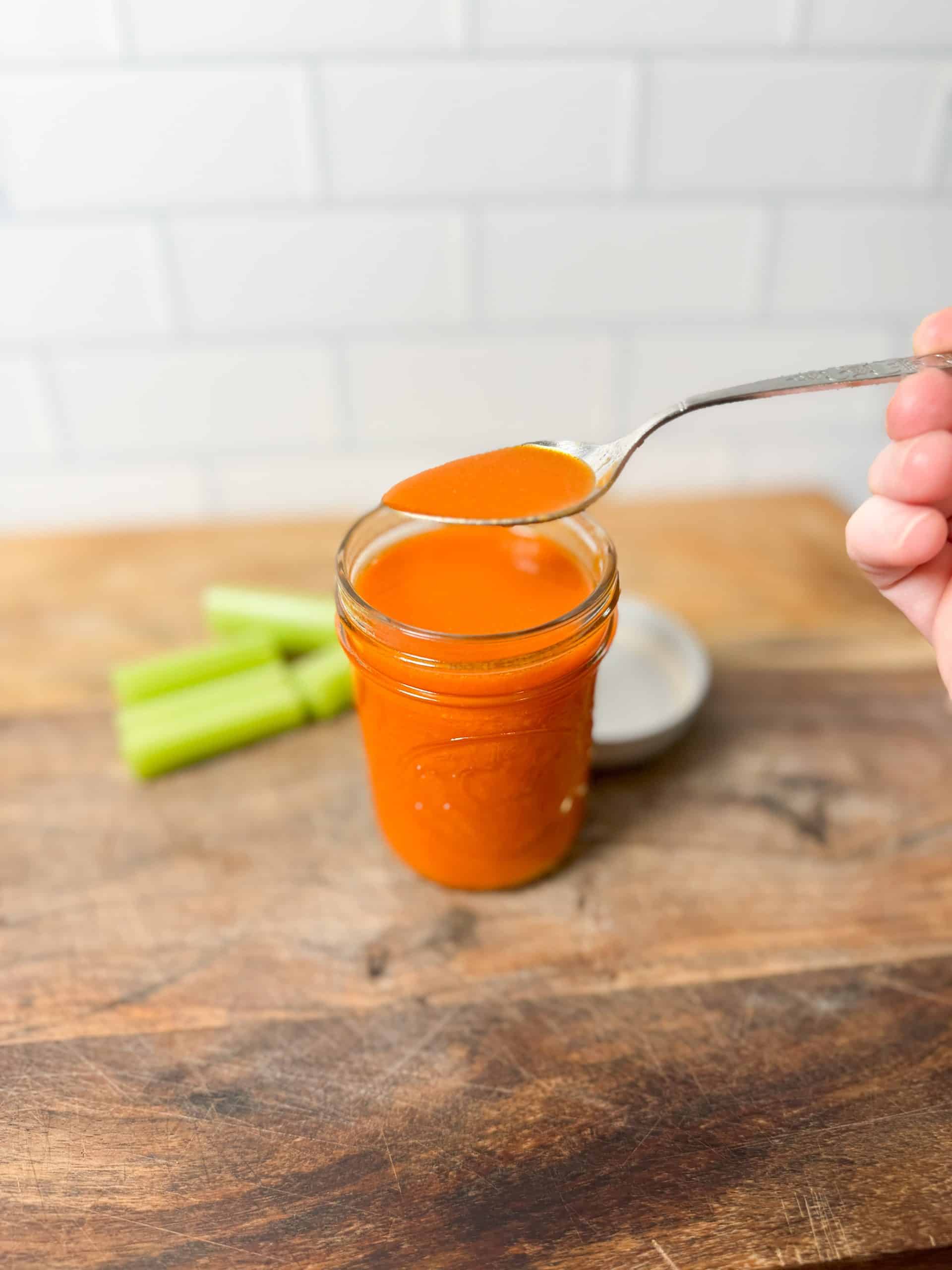 homemade buffalo sauce in a small mason jar sitting on a wooden cutting board next to some celery