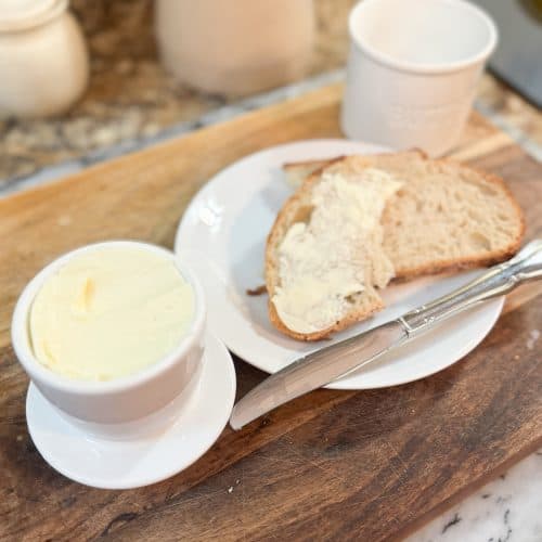 homemade cultured butter in a butter crock with a piece of sourdough bread buttered and sitting next to it on a woode cutting board
