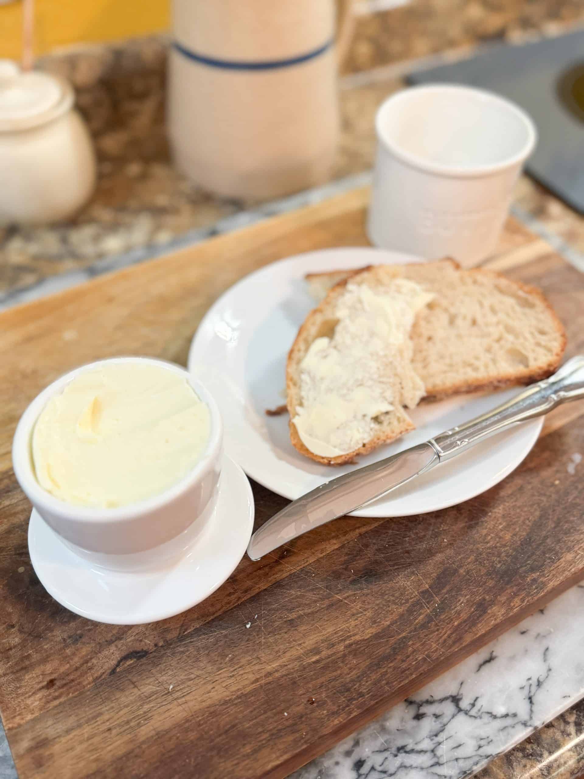 homemade cultured butter in a butter crock with a piece of sourdough bread buttered and sitting next to it on a woode cutting board