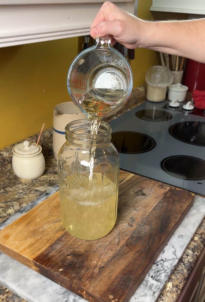 pouring white cranberry juice into a half gallon mason jar