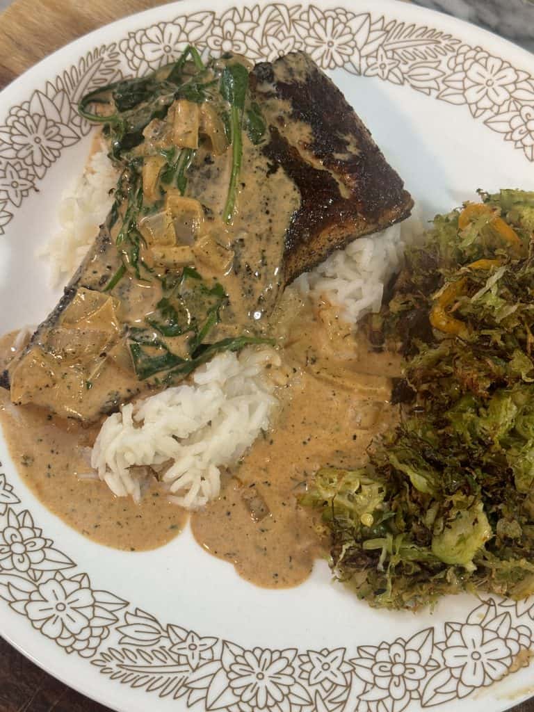 Pan-Seared Steelhead Trout in Creamy Tomato Spinach Sauce over a bed of rice served on a plate with brussels sprouts
