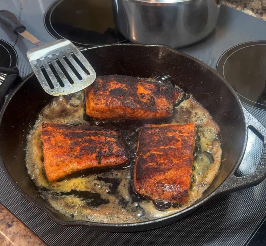 steelhead trout cooking in a cast iron pan flesh side up and seared