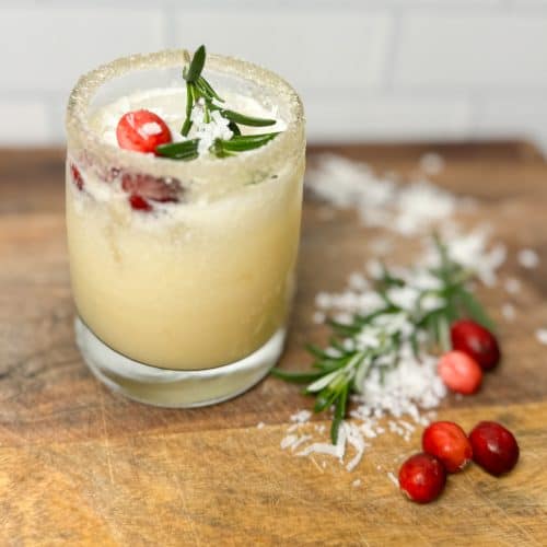 white cranberry punch on a wooden counter garnished with cranberrys, coconut shreds and rosemary sprigs