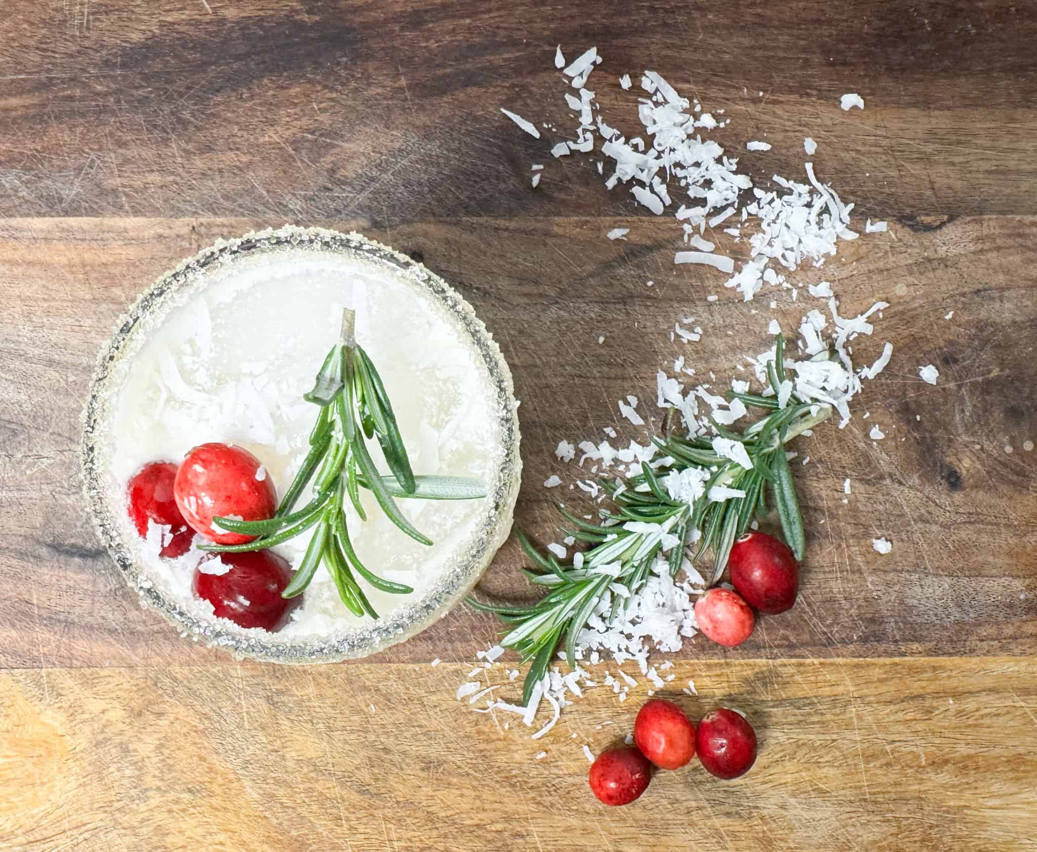 white cranberry punch on a wooden counter garnished with cranberrys, coconut shreds and rosemary sprigs