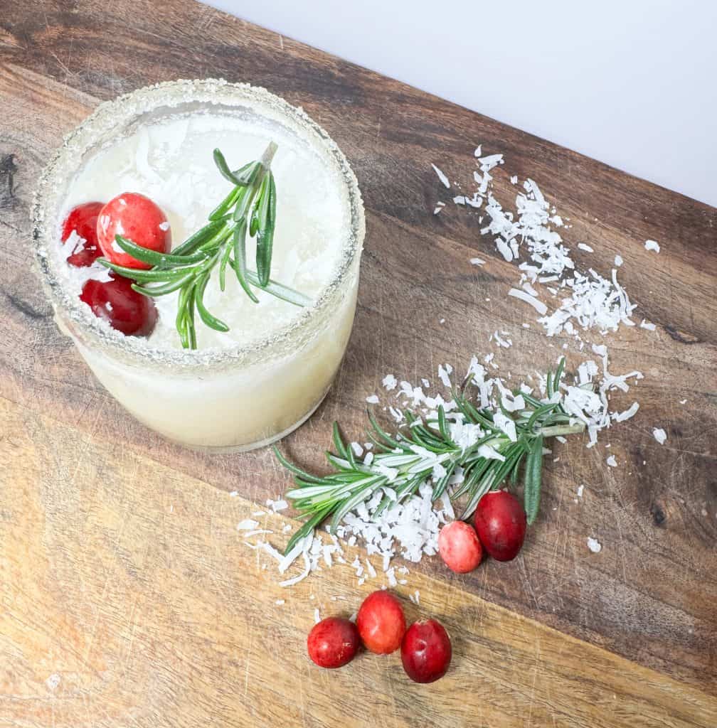 white cranberry punch on a wooden counter garnished with cranberrys, coconut shreds and rosemary sprigs