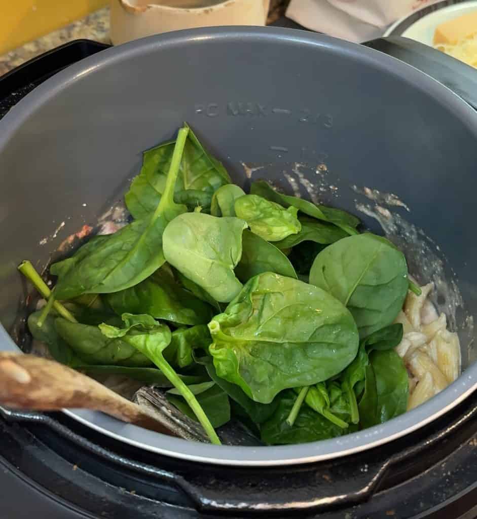 adding spinach to the Creamy Tomato and Sausage Pasta in an instant pot