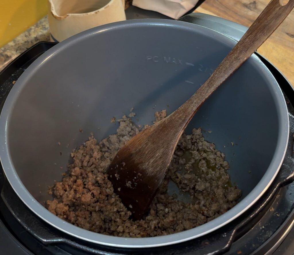 browning italian sausage in an instant pot with a wooden spoon
