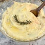 Instant Pot Creamy Garlic Mashed Potatoes in a large glass bowl with a wooden spoon and a sprig of rosemary
