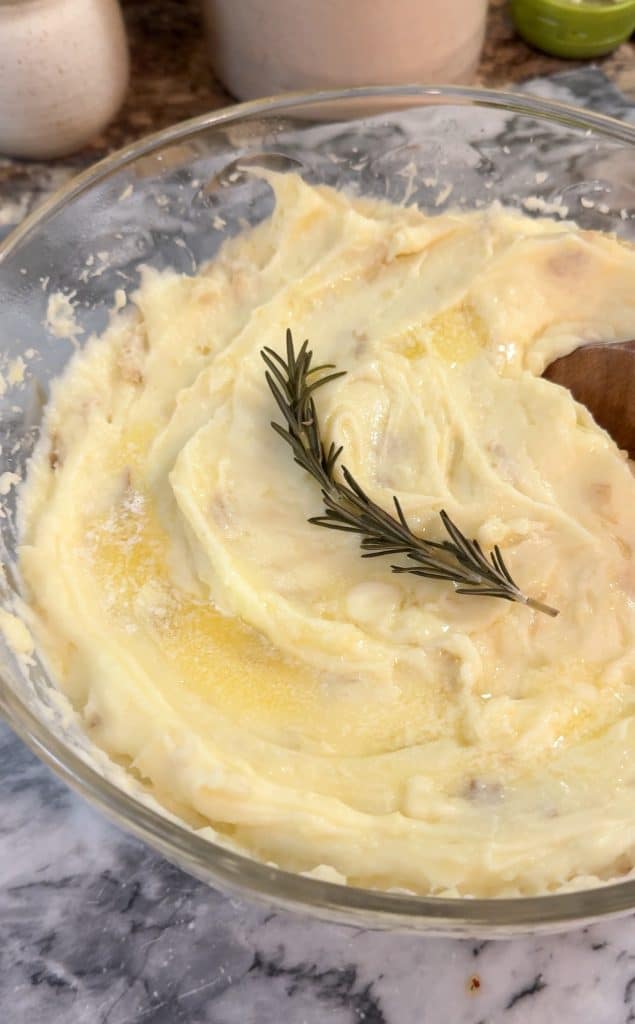 Instant Pot Creamy Garlic Mashed Potatoes in a large glass bowl with a sprig of rosemary on top