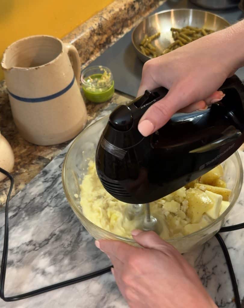 using a hand mixer to mix the cooked gold potatoes