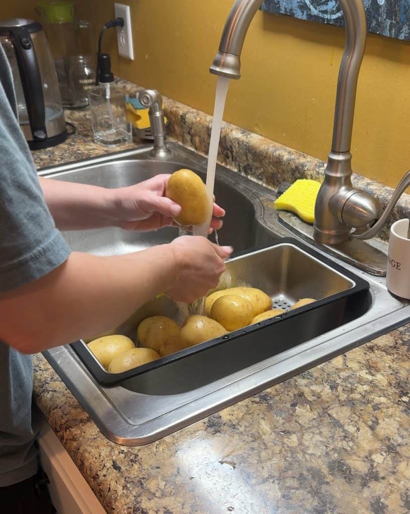 hand washing gold potatoes in a sink over a strainer