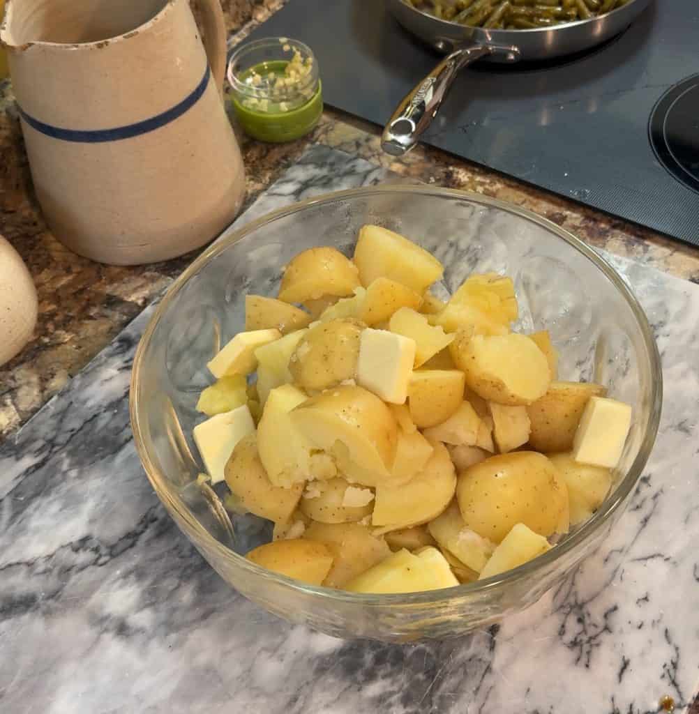 cubed gold potatoes fork tender in a large glass bowl with pats of butter on top