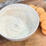 Greek Yogurt Ranch Dip in a white bowl sitting on a wood cutting board next to some crackers