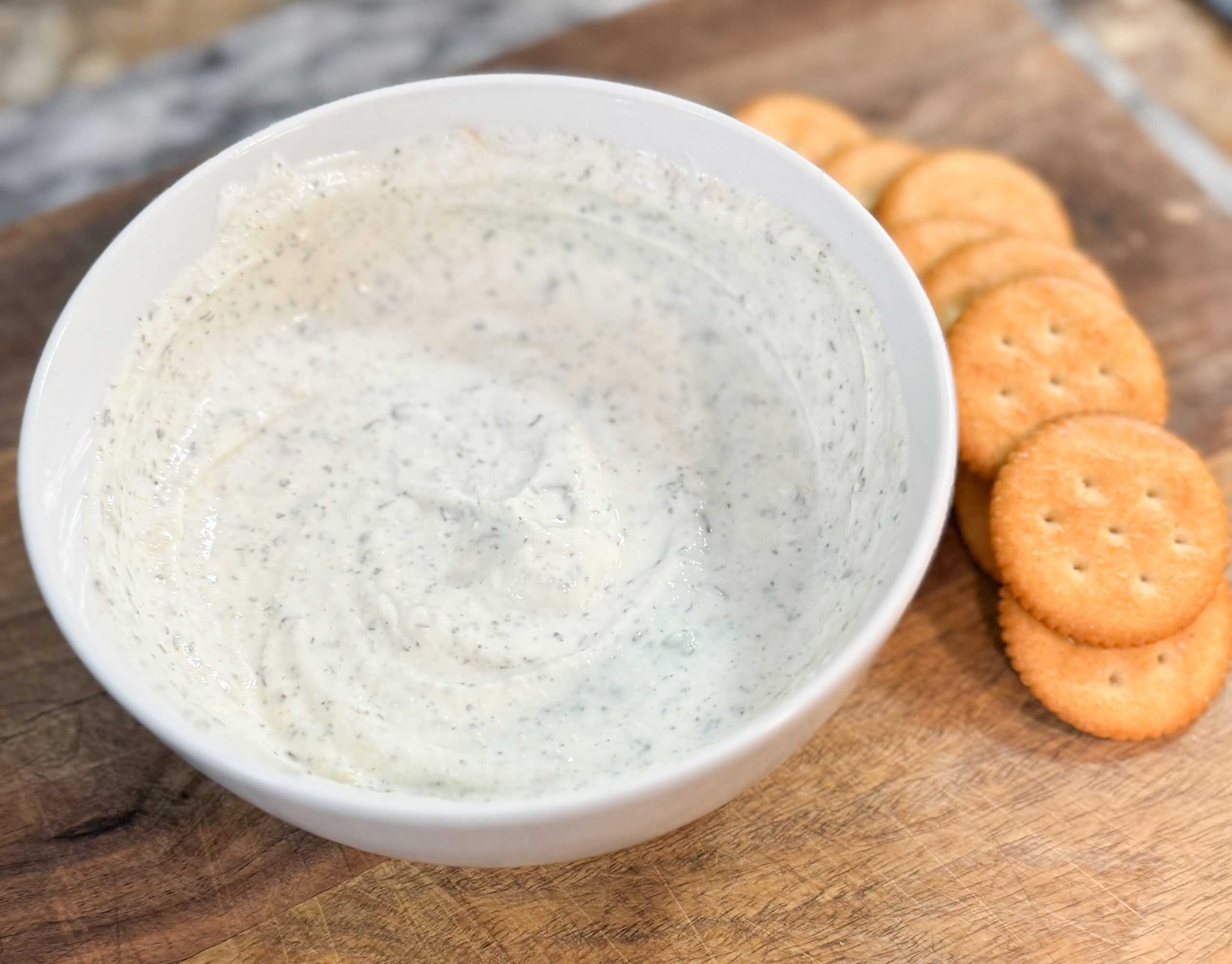 Greek Yogurt Ranch Dip in a white bowl sitting on a wood cutting board next to some crackers