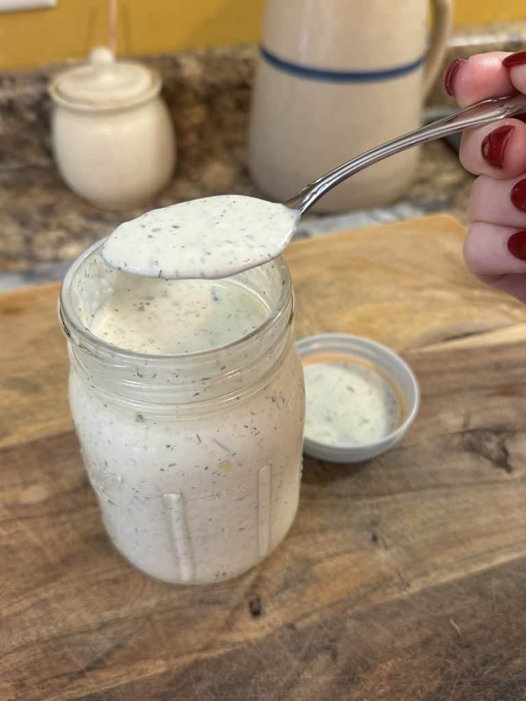 Homemade Ranch Dressing in a spoon over a mason jar on a wooden cutting board