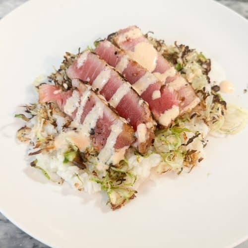 sliced ahi tuna steaks over a bed of rice and shredded brussels sprouts with a creamy sauce drizzled on top