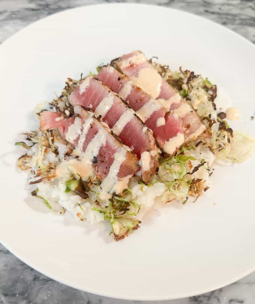 sliced ahi tuna steaks over a bed of rice and shredded brussels sprouts with a creamy sauce drizzled on top