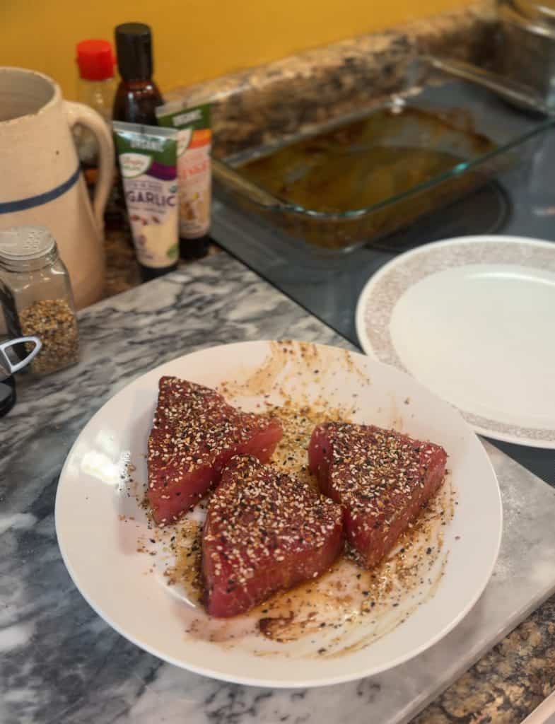 3 ahi tuna steaks coated in everything bagel seasoning sitting on a white plate