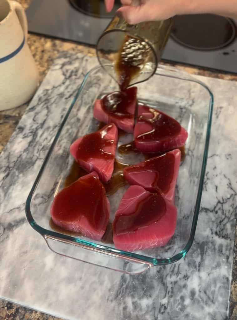 pouring marinade over 6 ahi tuna steaks in a glass dish