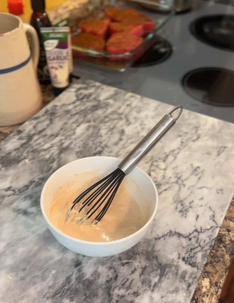a creamy sauce in a white bowl sitting on top of a marble board