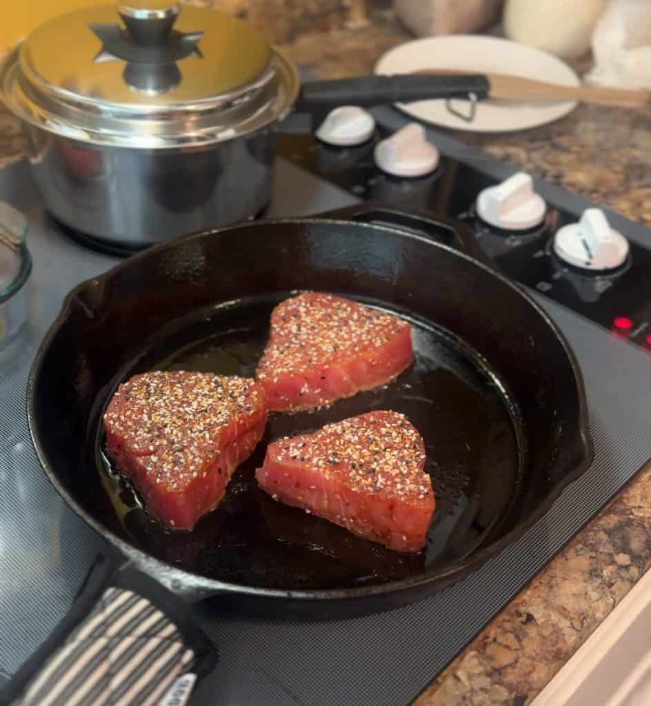 3 ahi tuna steaks coated in everything bagel seasoning searing in a hot cast iron skillet