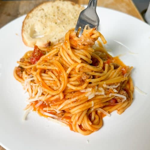 Instant pot spaghetti twisted up on a fork on a white plate next to a piece of toast
