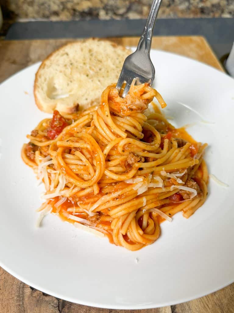 Instant pot spaghetti twisted up on a fork on a white plate next to a piece of toast