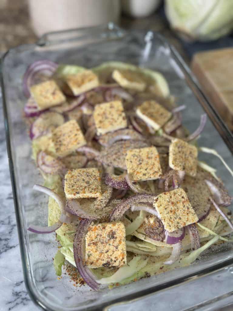 cabbage steaks and onion in a glass baking dish seasoned with salt and pepper and butter