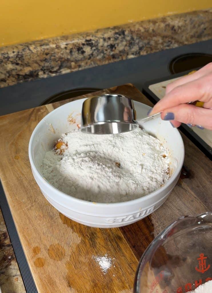pouring cake mix over the ingredients of peach cobbler